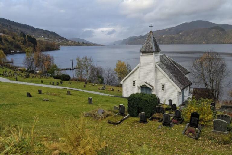 Oversiktsbilde med en hvit kirke i forgrunnen og fjorden bak. 