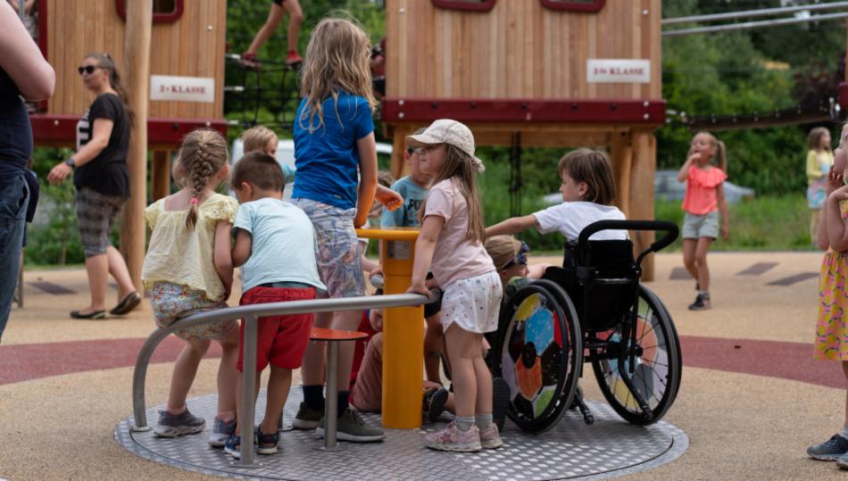 Barn på lekeplass. Ett barn sitter i rullestol og er delaktig i leken.
