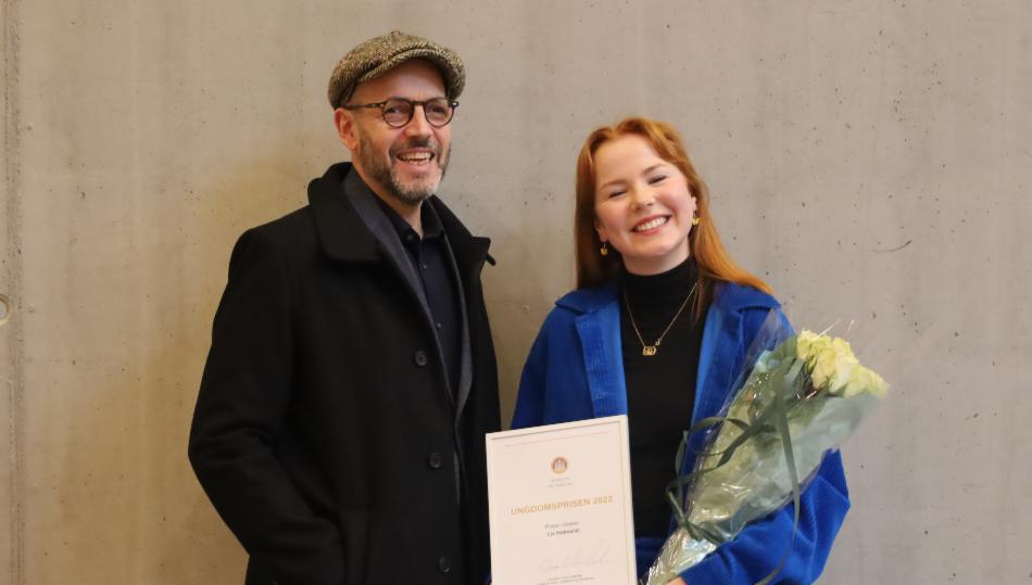 En mann og en jente smiler til kamera. Jenten holder en diplom og en blomsterbukett. 