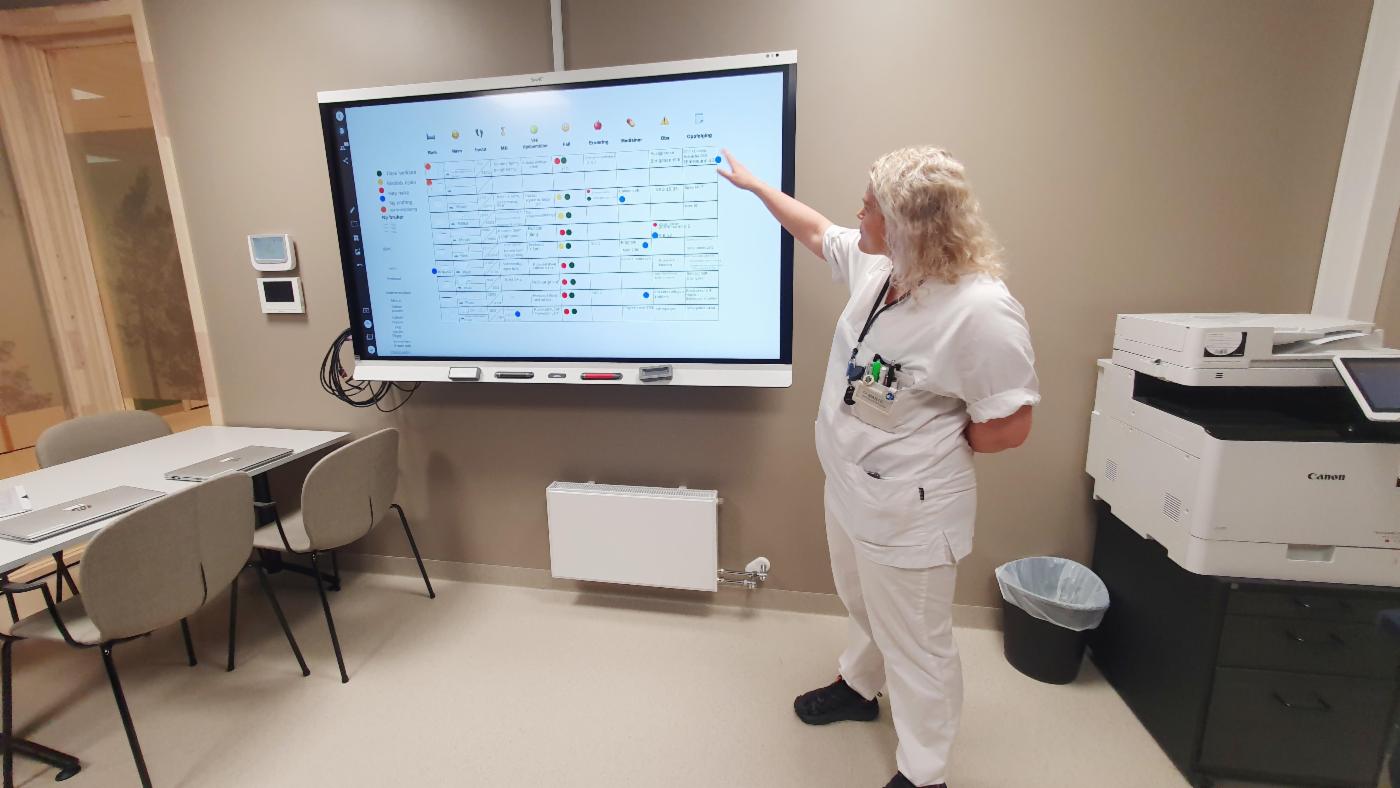 Sykepleier står foran digital tavle som brukes i pasientarbeidet