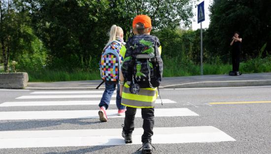 To små barn med skolesekk på ryggen går på et gangfelt.