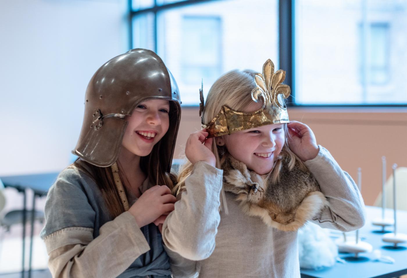 To barn på et museum som prøver vikinghjelmer. 