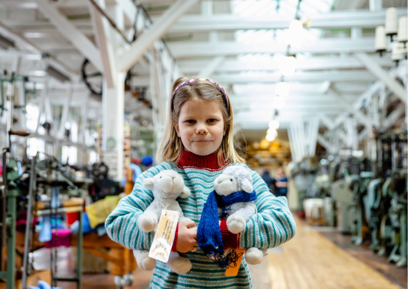 En jente står i en museumshall med to saue-bamser i hendene. 
