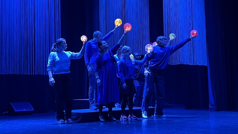 Dansere i blått lys på scenen med lysende kuler i hendene.