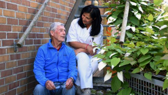 Bildet viser eldre beboer sammen med helsepersonell, sittende i en trappe. 