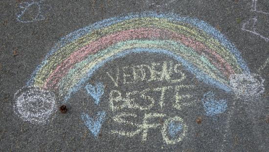 Regnbue og 'Verdens beste SFO' skrevet  med kritt på asfalt.