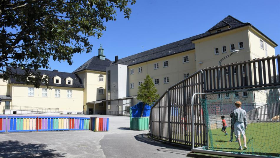 Gul skolebygning, ballbinge til høyre og fargerikt gjerde til venstre.