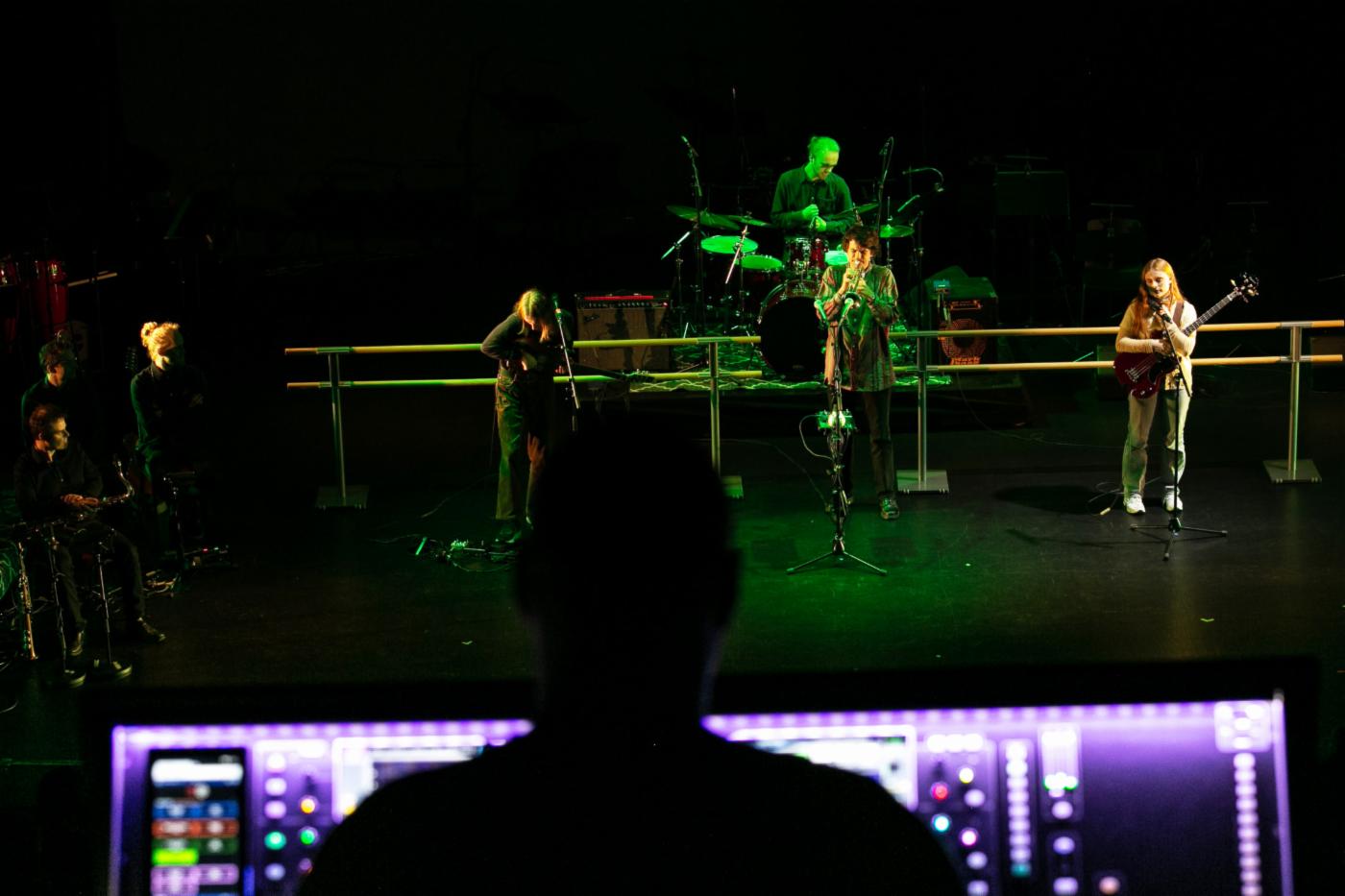 Bildet viser et band som spiller på en scene, i forgrunnen ser du konturene av en tekniker foran en skjerm med ryggen til