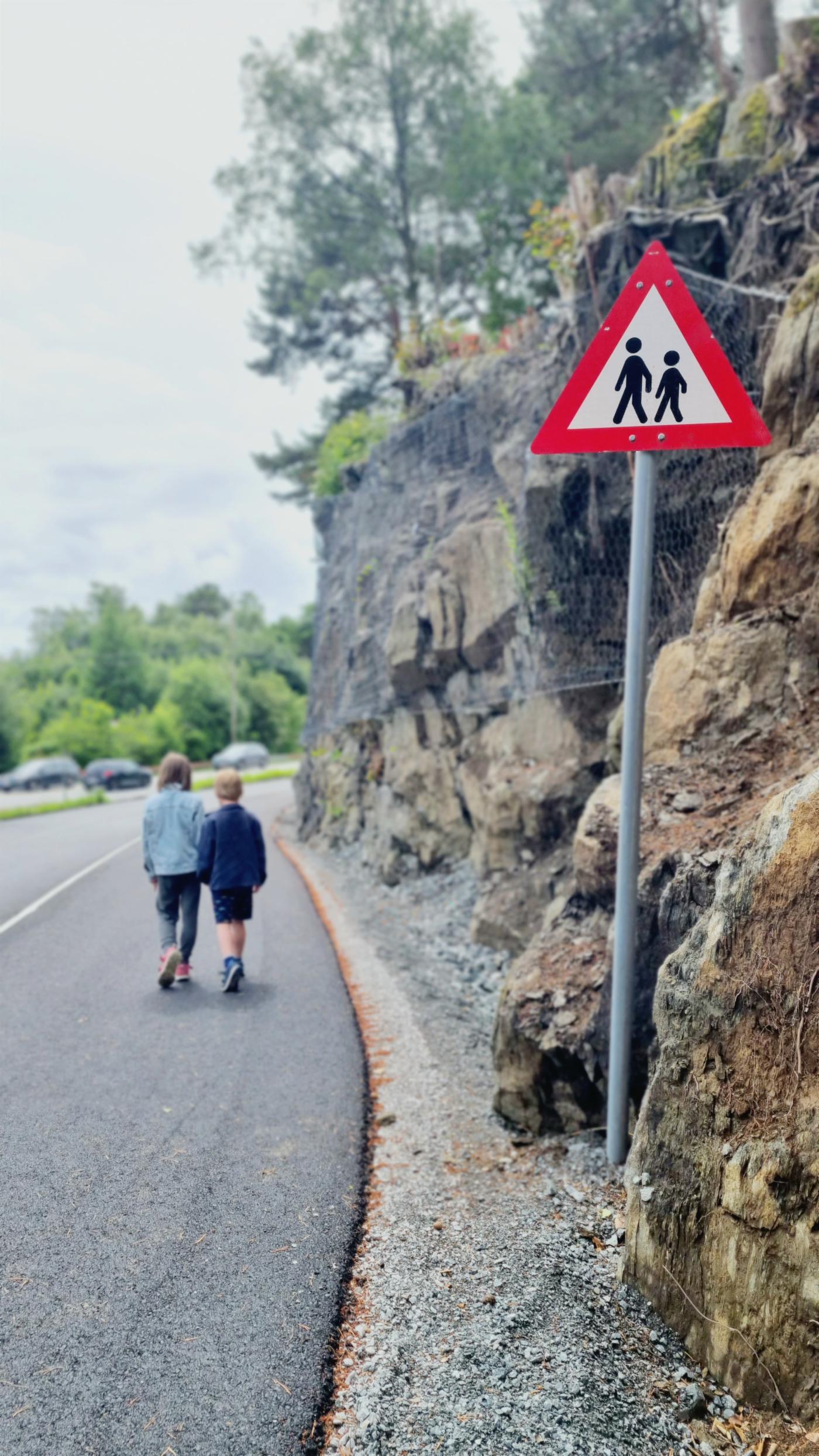 To barn går langs veien foran fareskilt barn