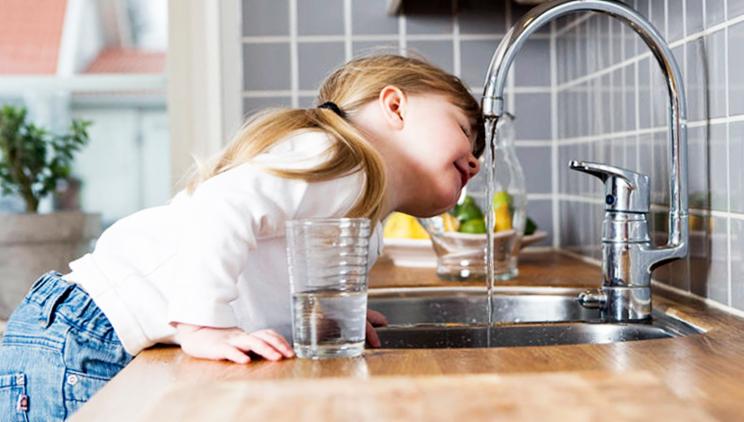 Jente drikker vann fra kjøkkenkran